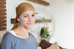 Portrait of young positive adult female cancer patient sitting in living room, smiling.