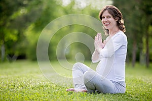 Portrait of young pregnant model meditating on grass lawn