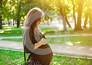 Portrait of young pregnant woman looking at her belly in a park