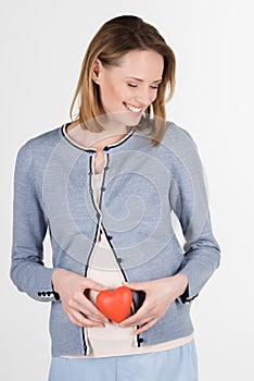 portrait of young pregnant woman with red heart in studio