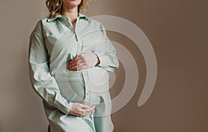 portrait of a young pregnant woman standing on a gray wall background and touching her stomach.