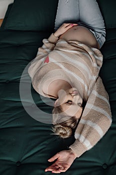 Portrait of young pregnant woman wearing beige sweater with application of heart, jeans, lying with closed eyes on bed.