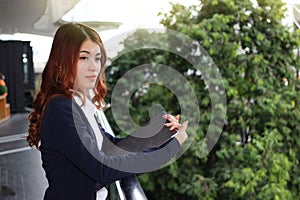 Portrait of young pretty Asian business woman holding clipboard and looking far away at public outdoor background.