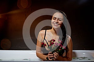 Portrait of young pretty brunette woman in bath with water and flowers in a dark room