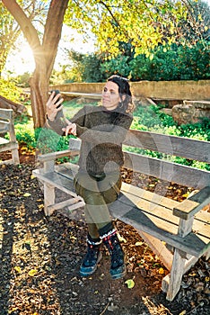 Portrait of a young pretty caucasian girl sitting on a park bench taking a selfie at sunset