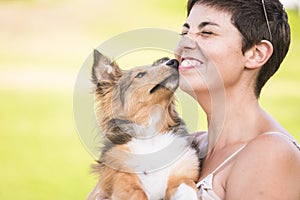 Portrait of young pretty caucasian woman enjoy and laugh while youth beautiful shetland dog puppy kiss her - concept of best