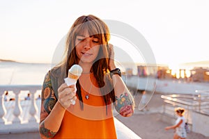Portrait of young pretty Caucasian woman with tattoos holds ice cream at sunny beach. Concept of freedom and summer
