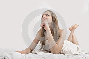 Portrait of young pretty dreaming woman in bed. Beautiful naked caucasian girl is covered with sheet. White background. Copy space