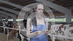 Portrait of young pretty female worker on the cow farm counting money smiling. Positive farmer gets income from her farm