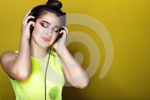 Portrait of young pretty girl with colourful artistic make-up and updo hair listening to the music in headphones and smiling