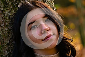 Portrait of a young pretty girl leaning her head against a tree trunk