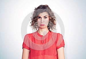 Portrait of a young pretty girl in a red dress with an emotional expression of resentment, on light background.