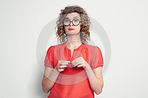 Portrait of a young pretty girl in a red dress and glasses with an emotional expression of resentment. Pout her lips