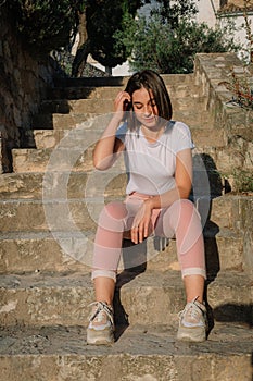 Portrait of young pretty girl sitting on stairs touching her short hair