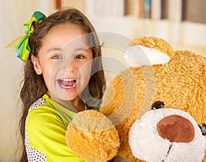 A portrait of a young pretty girl smiling and hugging her teddy bear over blurred background