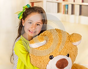 A portrait of a young pretty girl smiling and hugging her teddy bear over blurred background