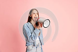 Portrait of young pretty girl, student in casual clothes shouting in megaphone against pink studio background. News