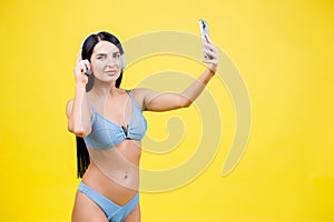 Portrait of young pretty girl with wireless headphones on head, taking selfie for social networks, smiling and laughing at phone