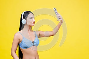 Portrait of young pretty girl with wireless headphones on head, taking selfie for social networks, smiling and laughing at phone