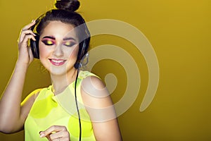 Portrait of young pretty model with colourful artistic make-up and updo hair listening to the music in headphones and smiling