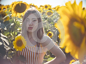 Portrait of young pretty woman agronomist standing on background of field with sunflowers, she looks at camera