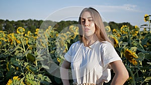 Portrait of young pretty woman agronomist standing on background of field with sunflowers, she looks at camera. copy space