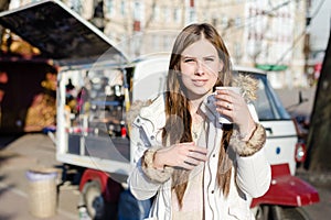 Portrait of young pretty woman with a cup of hot drink on sunny outdoors background