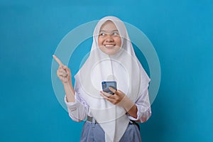 Portrait of young pretty woman student in uniform with hijab look aside pointing finger on copy space isolated on blue background