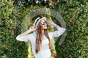 Portrait of young pretty woman in sunglasses and straw hat walking in green garden at vocation resort