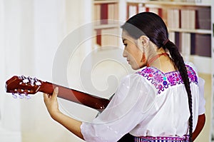 Portrait of young pretty woman wearing beautiful traditional andean clothing, sitting down with acoustic guitar playing