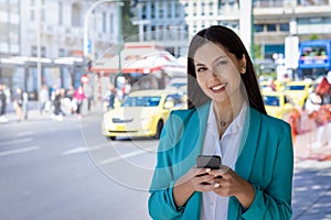 Portrait of a young, professional, Greek woman in corporate outfit holding her mobile