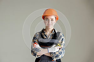 Portrait of a young professional woman electrician in a hard hat and overalls holding pliers for work, on a gray