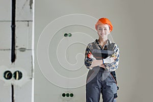 Portrait of a young professional woman electrician in a hard hat and overalls holding pliers for work, on a gray