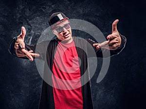 Portrait of a young rapper dressed in a hip-hop style, posing for a camera. Studio photo against a dark wall