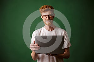 A portrait of young readhead man in white tshirt holding laptop