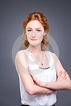 Portrait of a young redhaired beautiful girl in the studio on a gray isolated background. A woman is standing with her arms folded