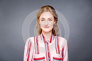 Portrait of a young red-haired beautiful girl in the studio on a gray isolated background. A woman stands and smiles in