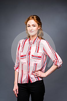 Portrait of a young red-haired beautiful girl in the studio on a gray isolated background. A woman stands and smiles in