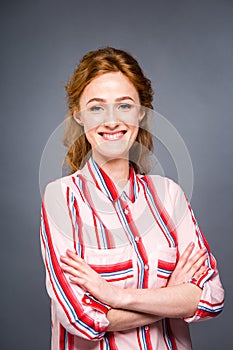 Portrait of a young red-haired beautiful girl in the studio on a gray isolated background. A woman stands and smiles in