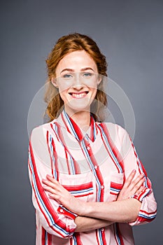 Portrait of a young red-haired beautiful girl in the studio on a gray isolated background. A woman stands and smiles in a red shir