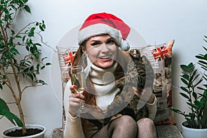 Portrait of young red haired woman in santa hat with cat and champange glass in home interior.