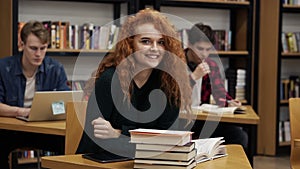 Portrait of a young red headed curly female student working on her thesis or preparing for exam. Reading a book sitting