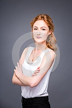 Portrait of a young redhaired beautiful girl in the studio on a gray isolated background. A woman is standing with her