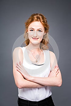 Portrait of a young redhaired beautiful girl in the studio on a gray isolated background. A woman is standing with her arms folded