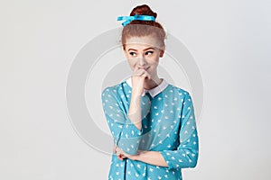 Portrait of young redhead female model having shy cute smile, holding hand on her lips, posing indoors.