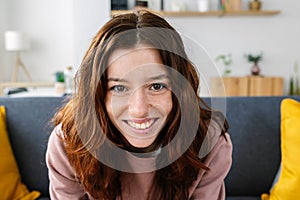 Portrait of young redhead girl smiling at camera sitting on sofa at home