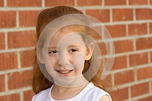 Portrait of Young redhead kid girl by brick wall