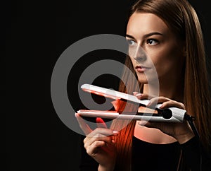 Portrait of young refined woman holding modern hair straightener in hands and looking aside at copy space photo