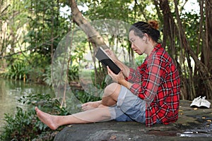 Portrait of young relaxed man in red shirt reading a book in beautiful nature background.