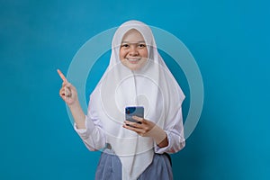 Portrait of young relaxed smiling woman student with hijab holding mobile phone isolated on blue background